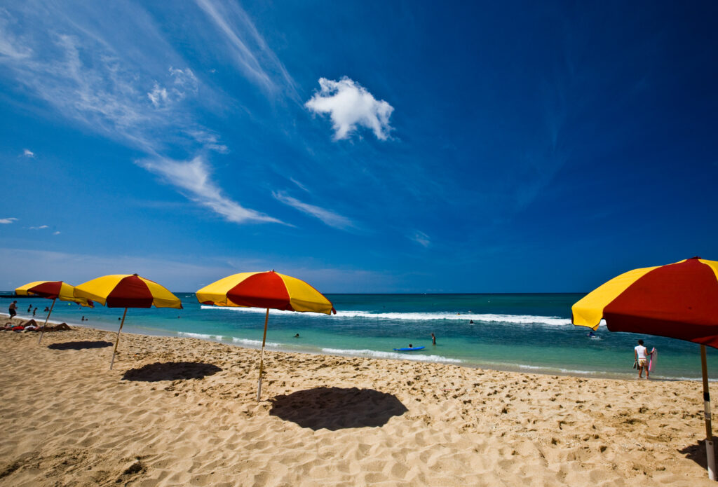 A beach with yellow and red umbrellas, a sunny blue skie and some waves