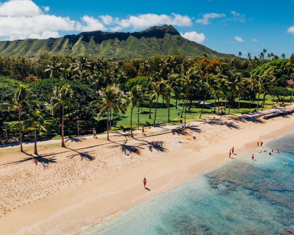 A long white sand beach with turquoise water and palm trees and a mountain in the background