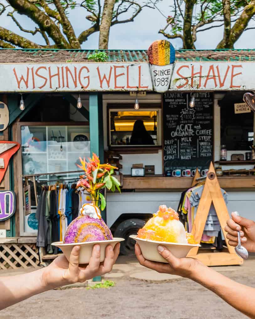 Shave ice held in front of a small shop that says Wishing Well Shave Ice