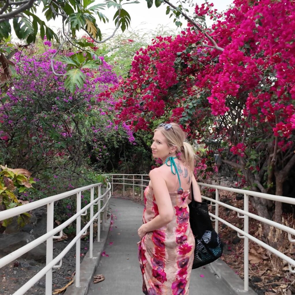 A blonde woman walking on a path with white rails surrounded by pink and purple flower