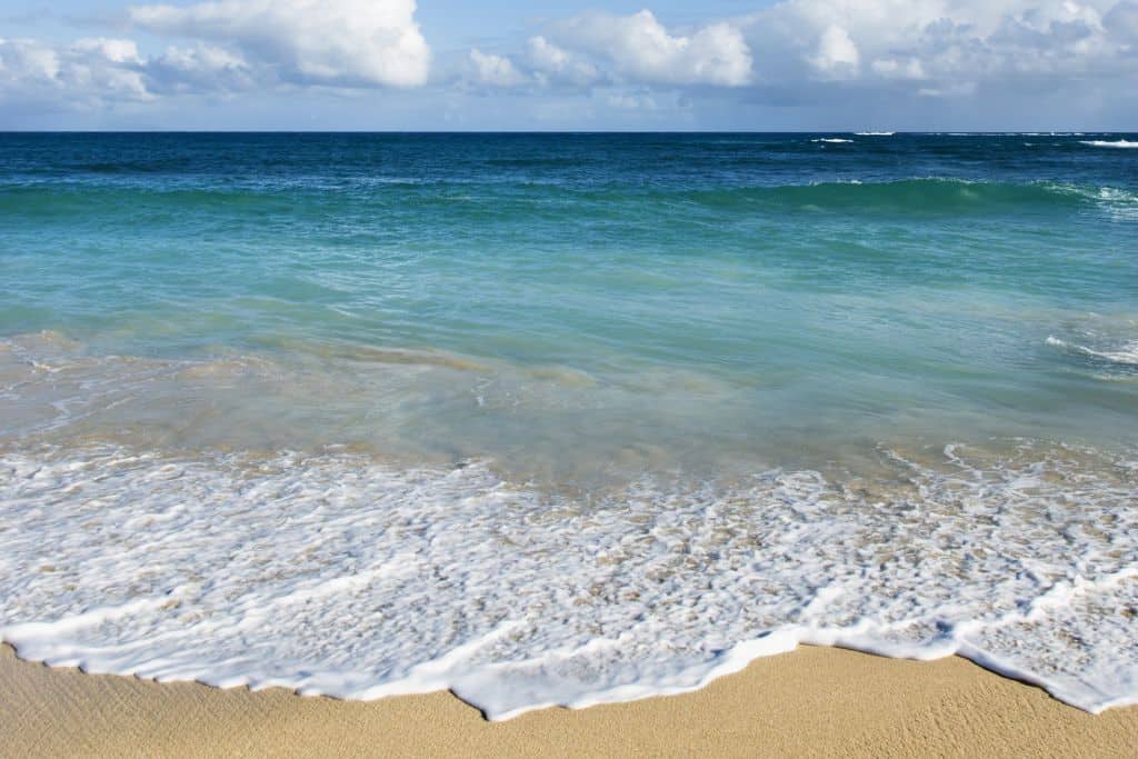 White and light turquoise waves lapping up on a yellow shore.