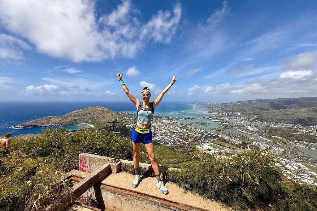 A brunette woman at the top of a high hike looking down to Oahu