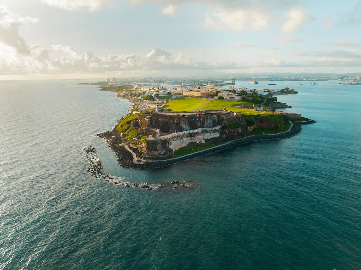 An aerial shot of an island with historical buildings on it and clouds in the sky.
