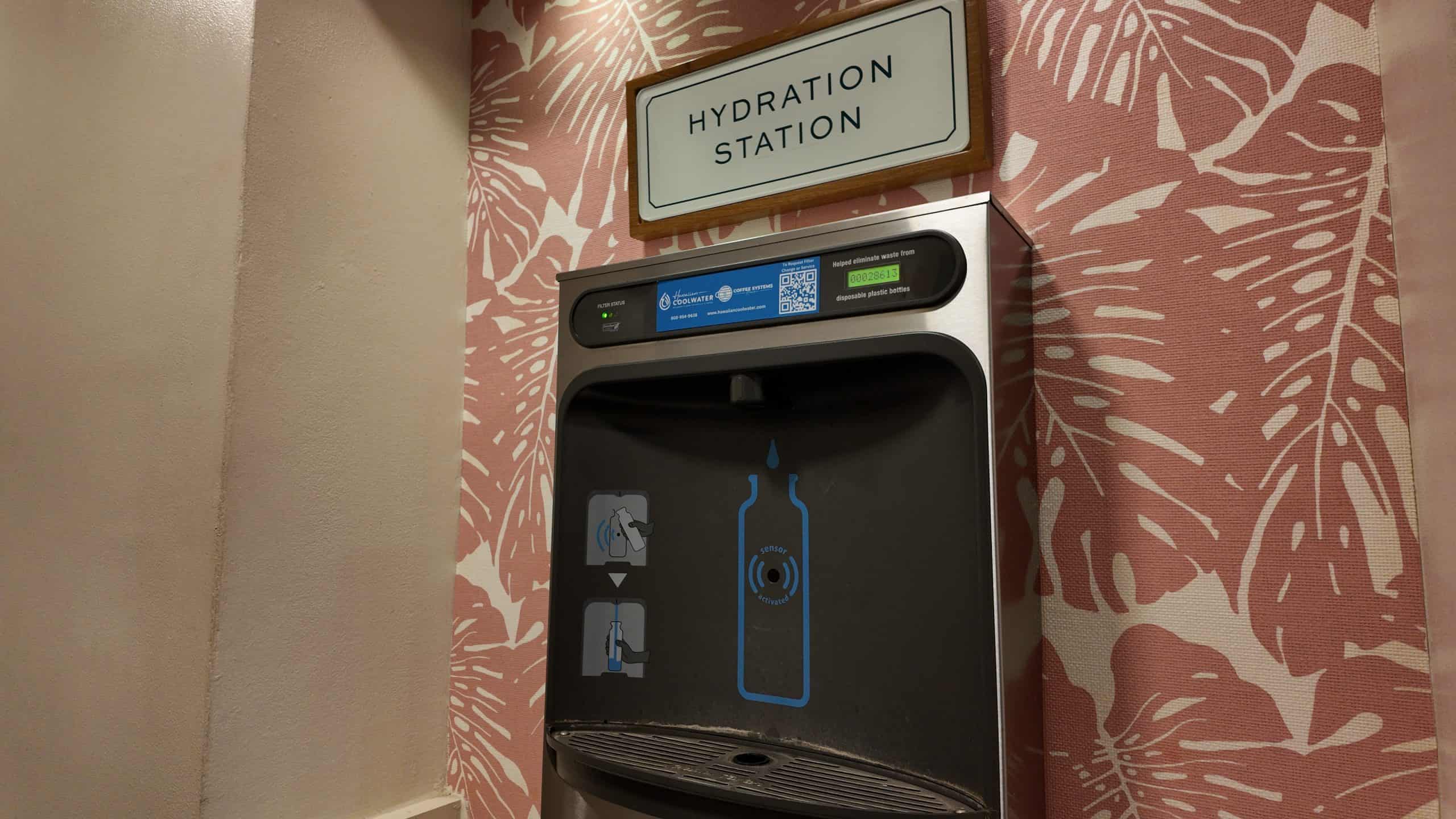 A filtered water hydration station against peach wallpaper in a hotel.