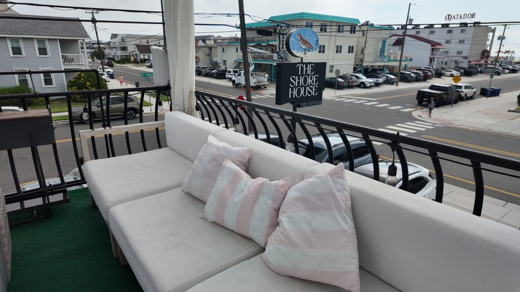 Outdoor furniture with pink and white striped pillows overlooking a hotel sign that says The Shore House