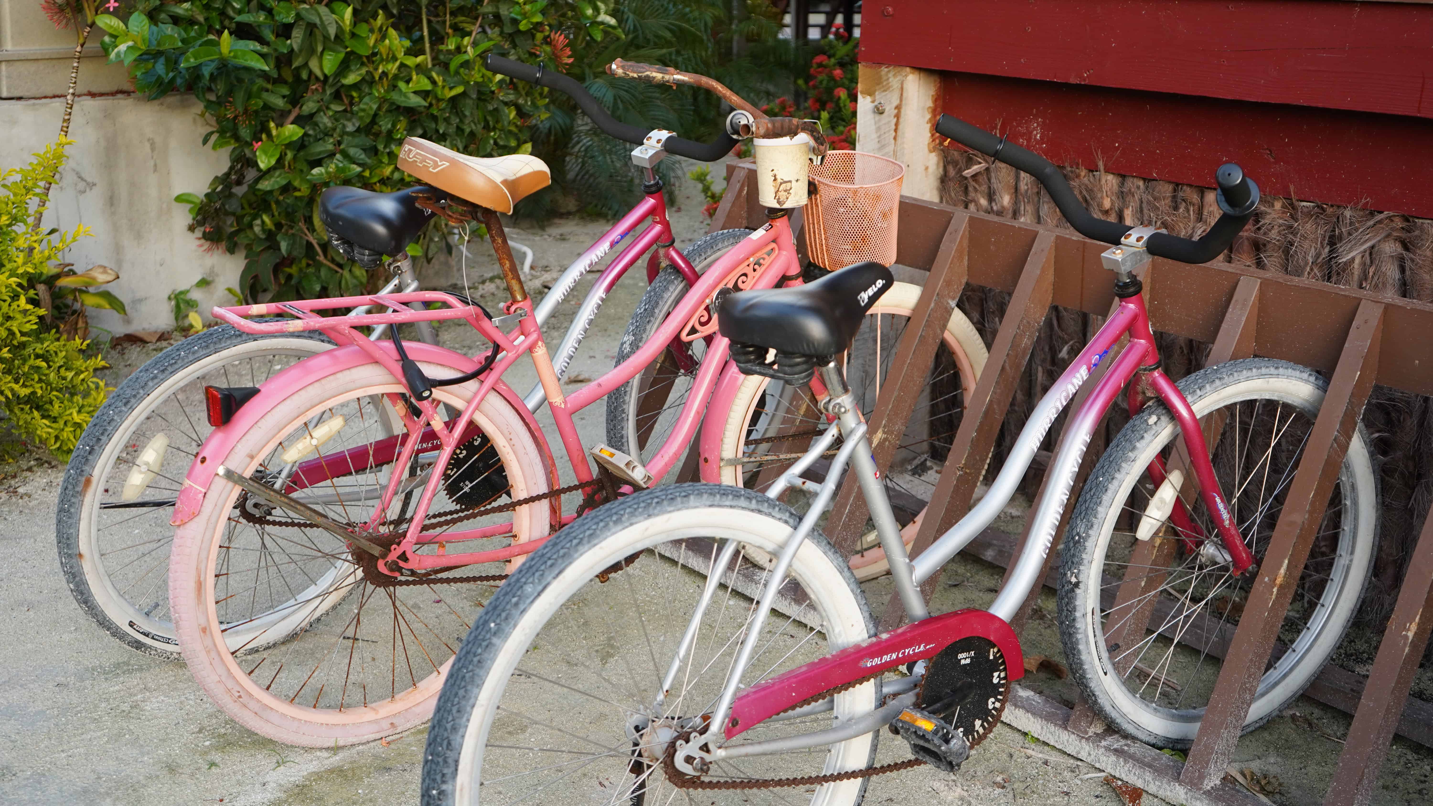 Three old pink and red bicycles with baskets linked up at a bike rack