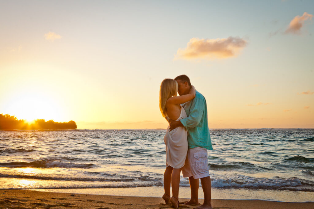 blonde-woman-in-white-dress-hugging-man-in-turquoise-shirt-and-white-shorts-on-beach-in-kauai-hawaii