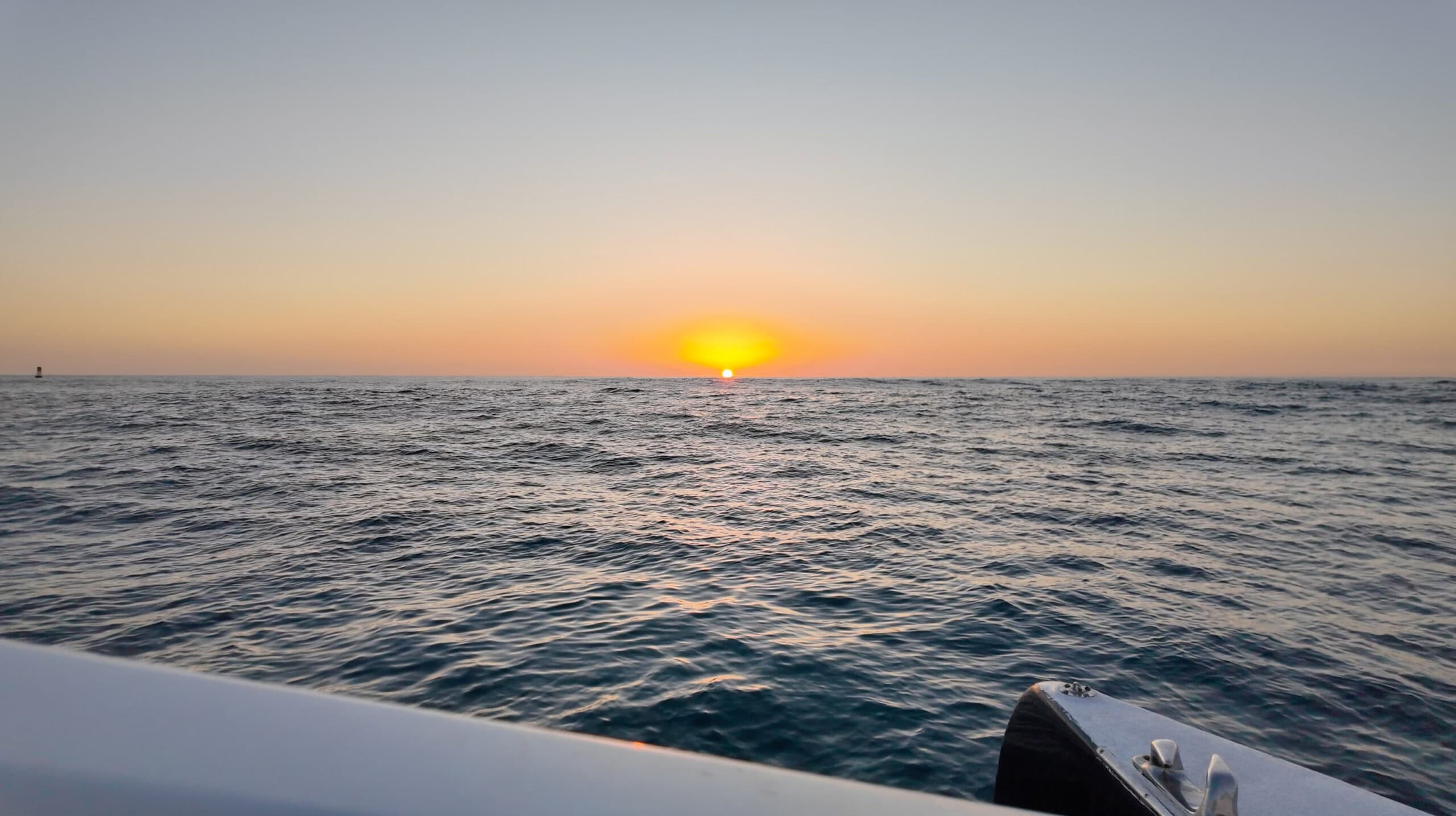 A view from a white boat of the sun setting in the ocean.